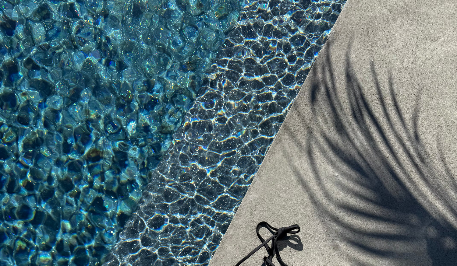 Black bikini set on a poolside concrete edge with clear blue water.